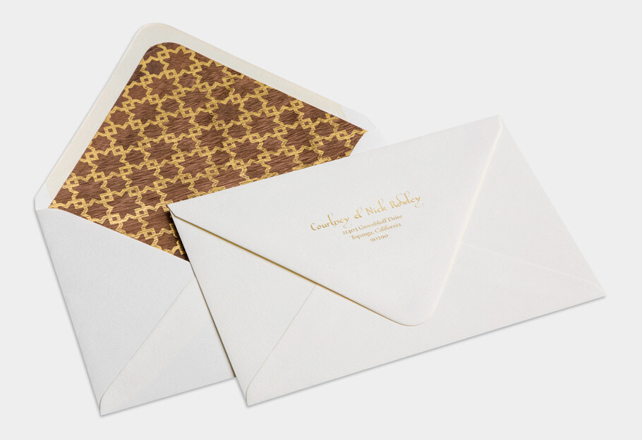Elegant white wedding envelopes with gold foil addressing and a geometric gold patterned liner, styled in an overlapping flat lay on a light gray background.