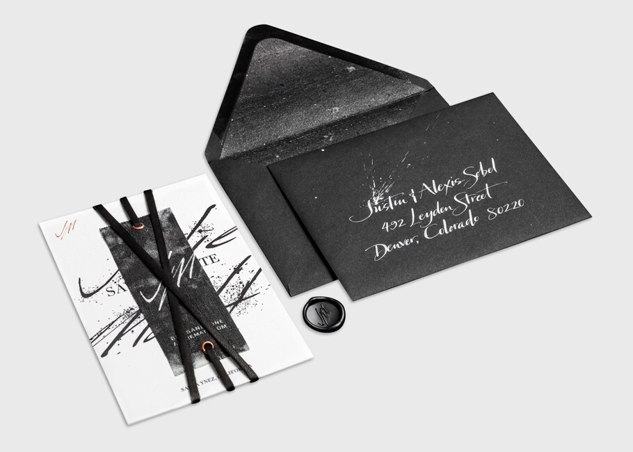 Moody black wedding invitation suite with white calligraphy, black velvet ribbon detailing, a wax seal accent, and a shimmering black envelope for a dramatic modern aesthetic.