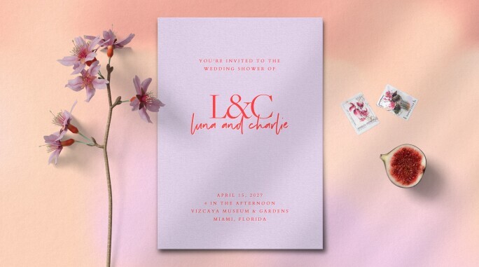 Modern wedding shower invitation featuring soft lavender cardstock with bright coral typography, styled with pink cherry blossoms, floral postage stamps, and a sliced fig on a blush pink background for a romantic spring aesthetic.